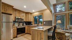 A kitchen with wooden cabinets, stainless steel appliances, a large island, and a view of trees through the windows. - 3BR Slopeside Disciples Village Condo 604 - Ski In/Ski Out on Boyneland! (Boyne Falls)