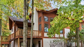 A two-story log cabin with a balcony, surrounded by trees with autumn foliage. - 3BR Slopeside Disciples Village Condo 604 - Ski In/Ski Out on Boyneland! (Boyne Falls)