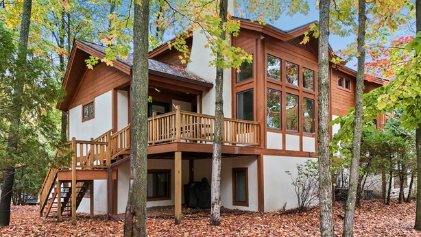 A two-story wooden cabin with a balcony, surrounded by trees and covered in autumn leaves. - 3BR Slopeside Disciples Village Condo 604 - Ski In/Ski Out on Boyneland! (Boyne Falls)