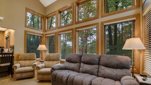 A spacious living room with a large sectional sofa, two armchairs, and a coffee table. There are multiple windows with blinds, allowing natural light to enter. - 3BR Slopeside Disciples Village Condo 604 - Ski In/Ski Out on Boyneland! (Boyne Falls)