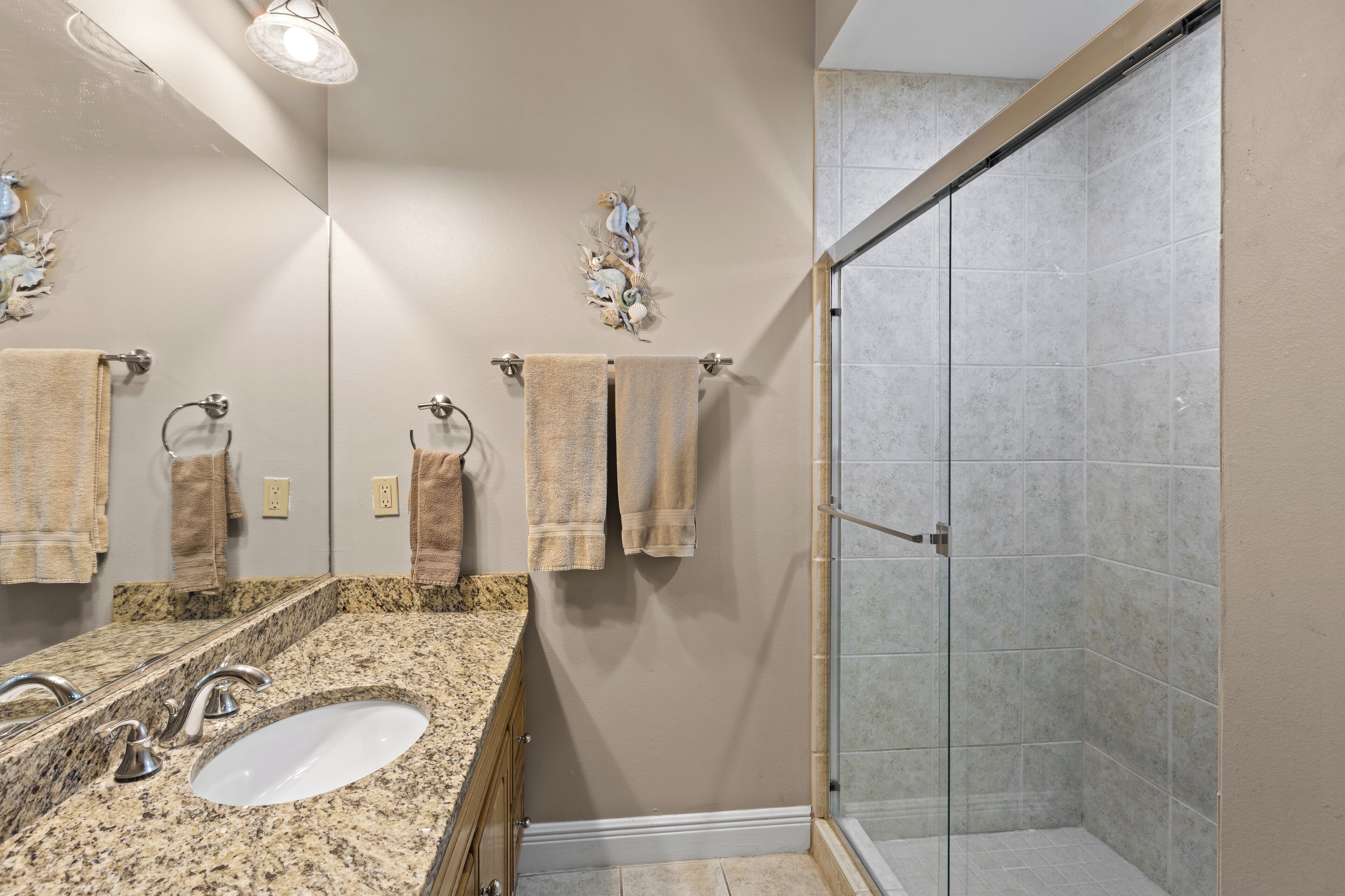 A bathroom with a granite countertop sink, two mirrors, and a glass-enclosed shower.
