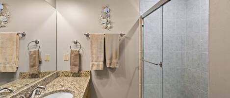 A bathroom with a granite countertop sink, two mirrors, and a glass-enclosed shower.