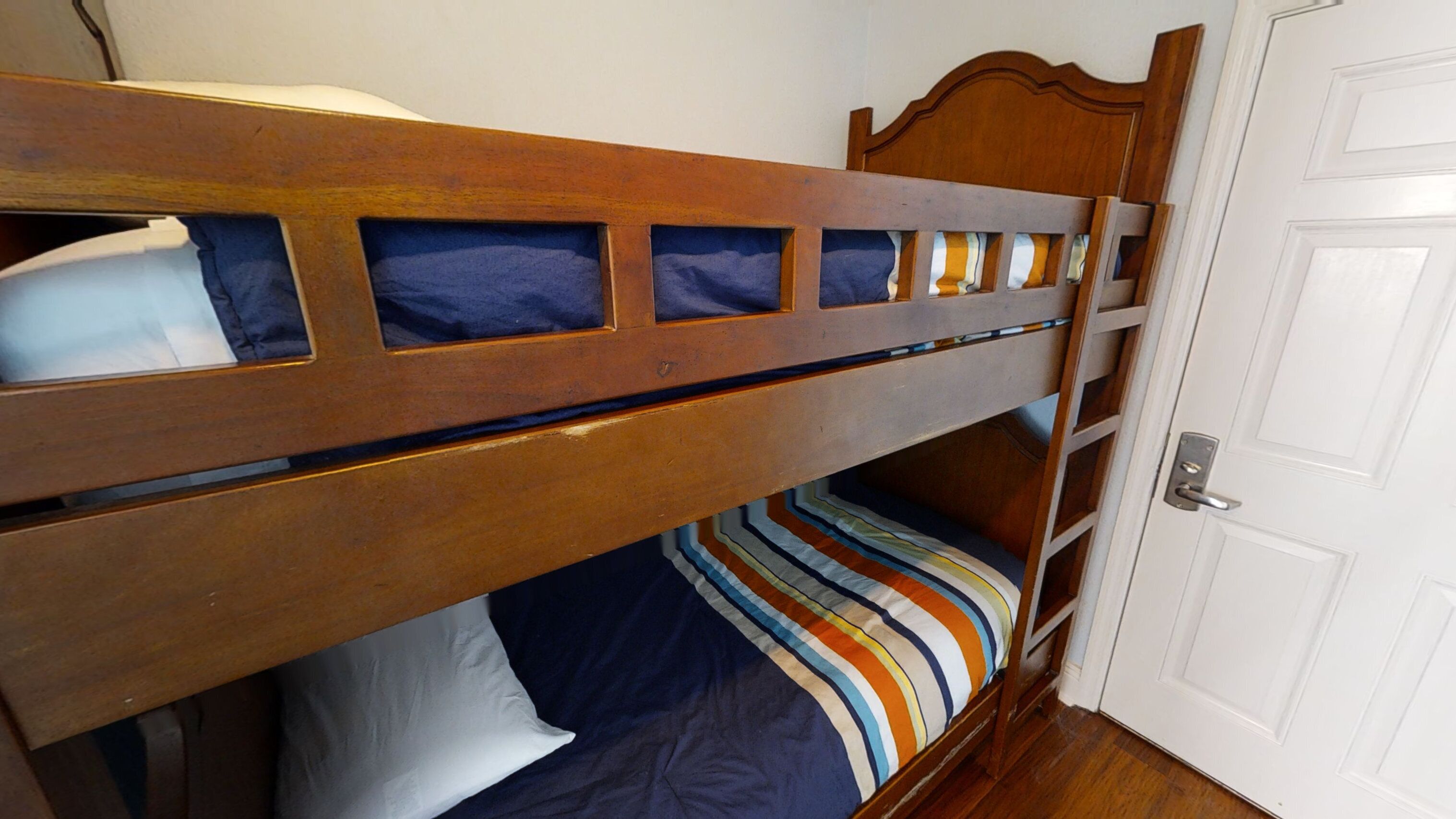 Un letto a castello con testiera in legno, copripiumino a righe e una porta bianca sullo sfondo.