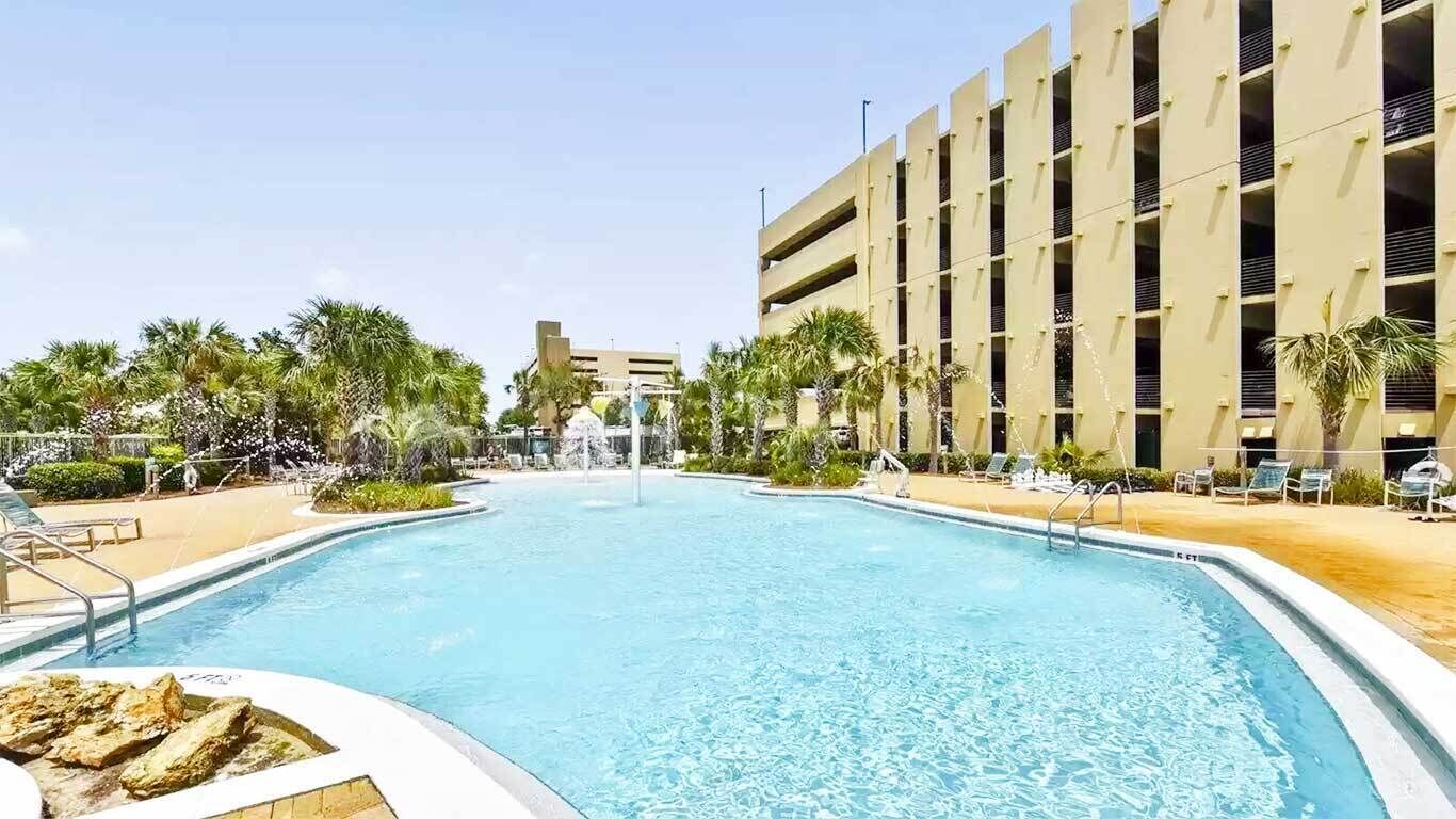 Una piscina rodeada de palmeras y un edificio con varios balcones.