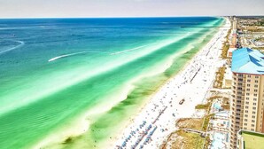 An aerial view of a beach with a pier extending into the ocean, a hotel with a blue roof, and a pool area with umbrellas. - Gulf Front Main Bedroom Free round of Golf & Activities Every Day! (Panama City Beach)