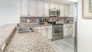 A kitchen with white cabinets, a granite countertop, stainless steel appliances, and a backsplash. - Bay View Villas 107 | Waterfront, Community Pool (Tybee Island)