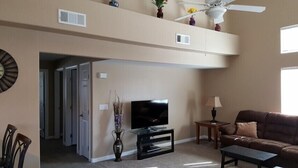 A living room with a flat-screen TV on a black stand, a brown leather sofa, a small wooden side table, and a ceiling fan. - Camellia Ridge by Mesquite Vacation Rentals with Community Amenities and $510 in free daily activities (Mesquite)