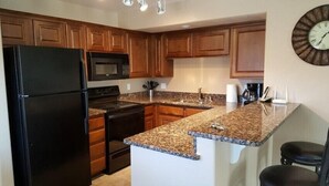 A kitchen with wooden cabinets, a black refrigerator, a microwave, a stove, a sink, and a granite countertop. - Camellia Ridge by Mesquite Vacation Rentals with Community Amenities and $510 in free daily activities (Mesquite)
