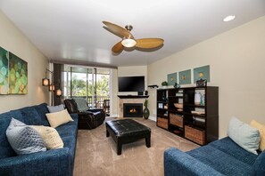 A living room with a ceiling fan, a fireplace, a television, and a bookshelf. - Luxury 1 bdrm condo in North Coast Village, garden view G202 North Coast Village (Oceanside)