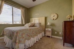 A bedroom with a bed, a nightstand, a wooden dresser, a wall clock, and a window with curtains.