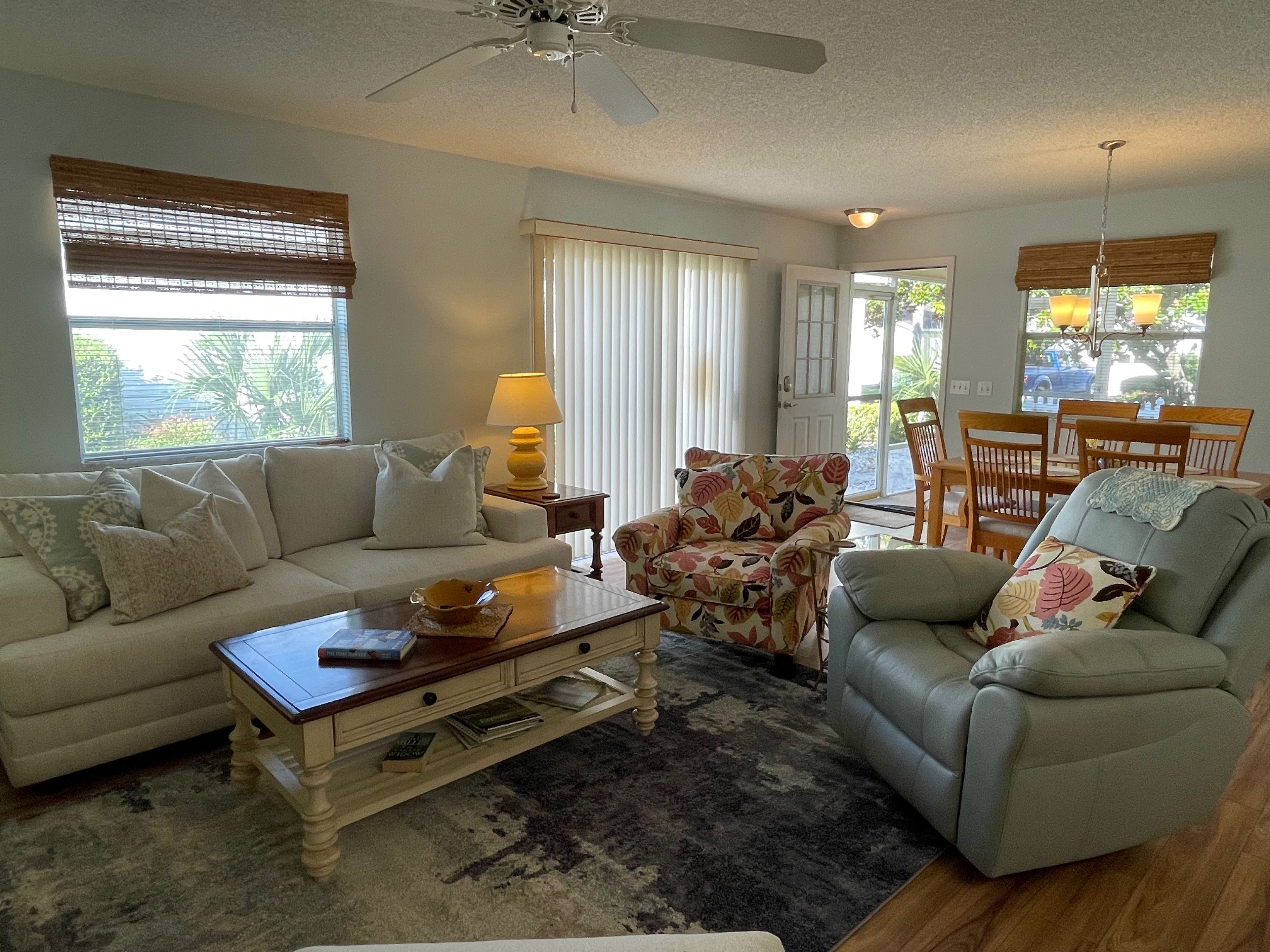 A living room with a sofa, armchair, coffee table, and a dining area with chairs and a table.