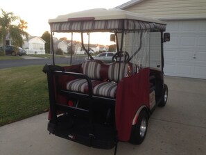 A golf cart parked on a driveway with a covered seating area and a rear storage compartment.
