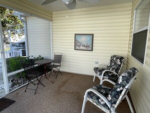 A covered patio with a table and chairs, a ceiling fan, and a painting on the wall.