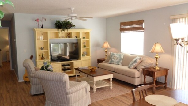 A living room with a television, a sofa, two chairs, a coffee table, and a ceiling fan. - AMAZING LOCATION! Beautiful 2/2 Patio Villa w/GOLF CART & WiFi Close to Town (The Villages)