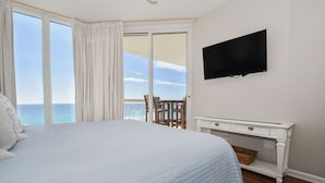 Une chambre avec un grand lit, un téléviseur fixé au mur, une petite table et une vue sur l’océan par une porte coulissante.