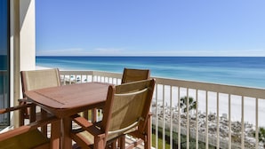 Une table et des chaises en bois sur un balcon avec vue sur l’océan et la plage.