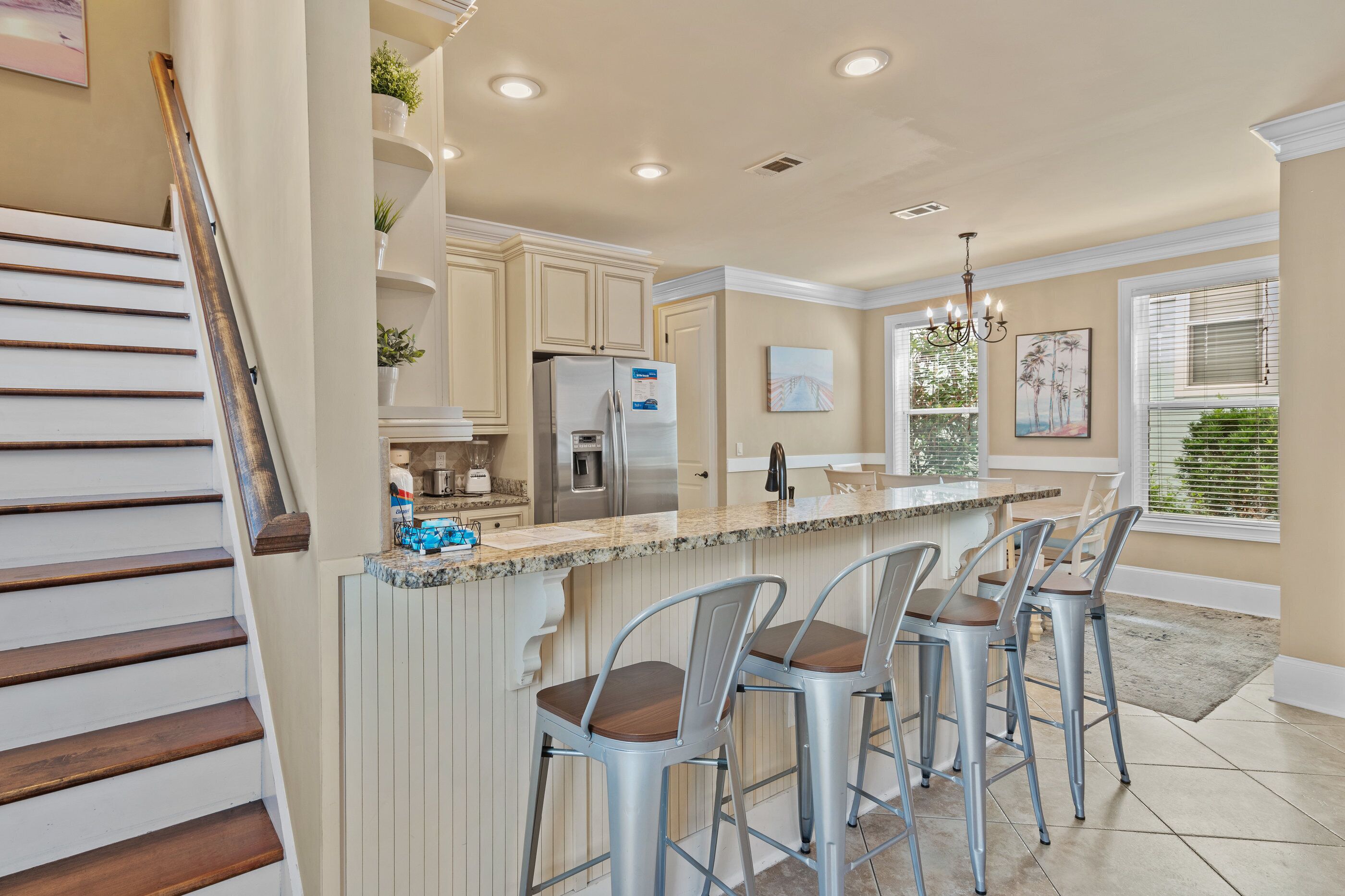 A kitchen with a central island, bar stools, a refrigerator, and a staircase.