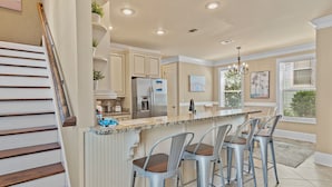 Una cocina con una isla central, taburetes de bar, un refrigerador y una escalera.