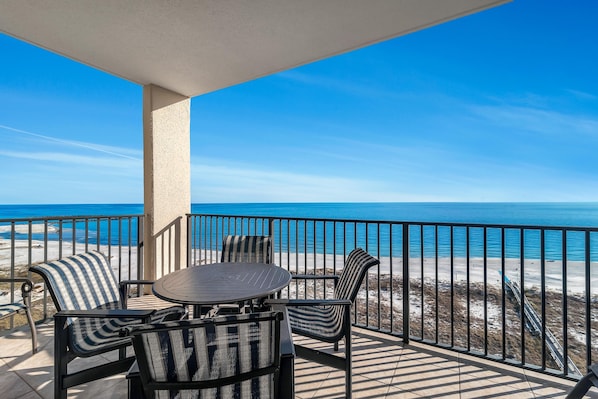 Un balcon avec une table et des chaises, donnant sur une plage et l’océan.