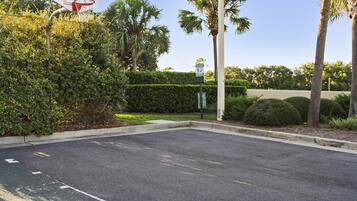 A parking lot with a basketball hoop, palm trees, and a sign indicating a pet waste area.