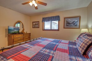 A bedroom with a bed, dresser, TV, and ceiling fan.