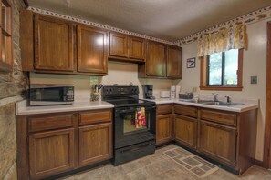 A kitchen with wooden cabinets, a microwave, stove, and a window with curtains.