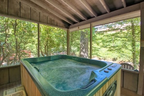 A hot tub with a wooden interior and a view of trees through large windows.