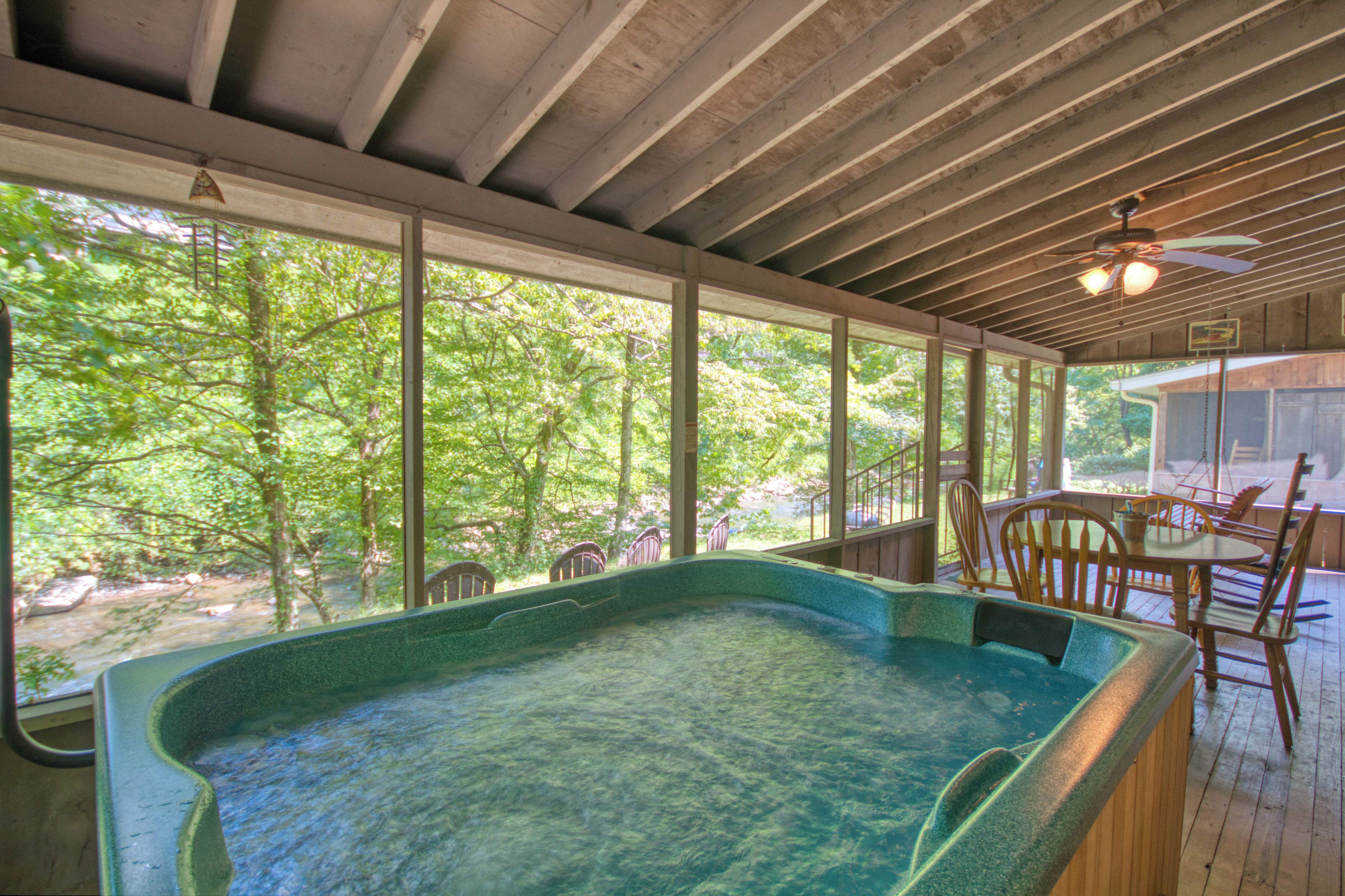 A hot tub in a covered outdoor area with wooden flooring, large windows, and a ceiling fan.