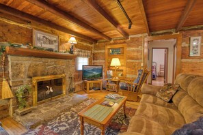 Un acogedor interior de cabaña de madera con chimenea de piedra, muebles de madera y un televisor.