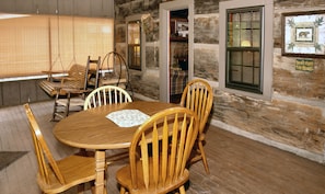 A wooden dining table with four chairs, a placemat, and a window with blinds.
