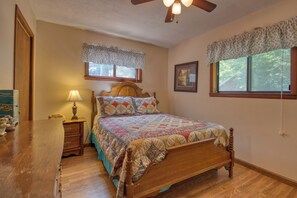 Un dormitorio con una cama de madera, una mesita de noche, una lámpara, un ventilador de techo y una ventana con un adornado de flores.