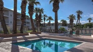 A swimming pool with lounge chairs, palm trees, and a building in the background.