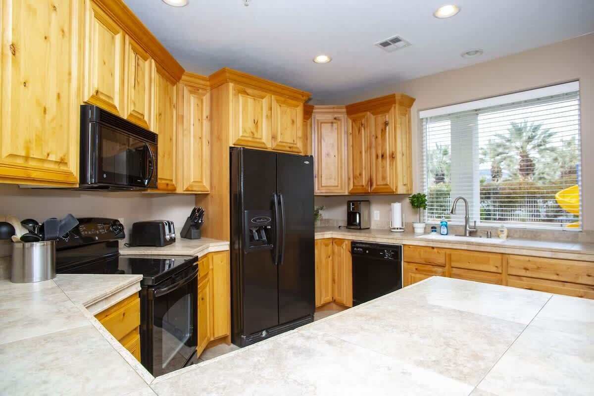 A kitchen with wooden cabinets, a black refrigerator, a microwave, a stove, and a window with blinds.