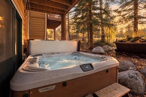 Een hottub buiten een blokhut met een houten terras, omringd door bomen en rotsen.