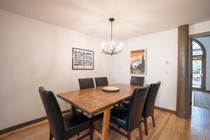 A dining room with a wooden table, six chairs, a chandelier, and two framed posters on the wall. - Elk Ridge Trail Townhome: Hot Tub, Spacious, Cool Location (Breckenridge)