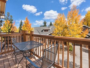 A wooden deck with a table and chairs, overlooking a residential area with autumn-colored trees.