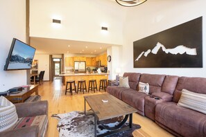 A spacious living area with a brown leather sofa, a wooden coffee table, and a mounted television. - Elk Ridge Trail Townhome: Hot Tub, Spacious, Cool Location (Breckenridge)