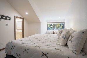 A bedroom with a large bed, a window with a view of trees, and a door leading to a bathroom. - Elk Ridge Trail Townhome: Hot Tub, Spacious, Cool Location (Breckenridge)