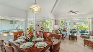 Un coin repas avec une table en bois dressée pour quatre personnes, entourée de chaises, et un coin salon avec un canapé et des fauteuils.