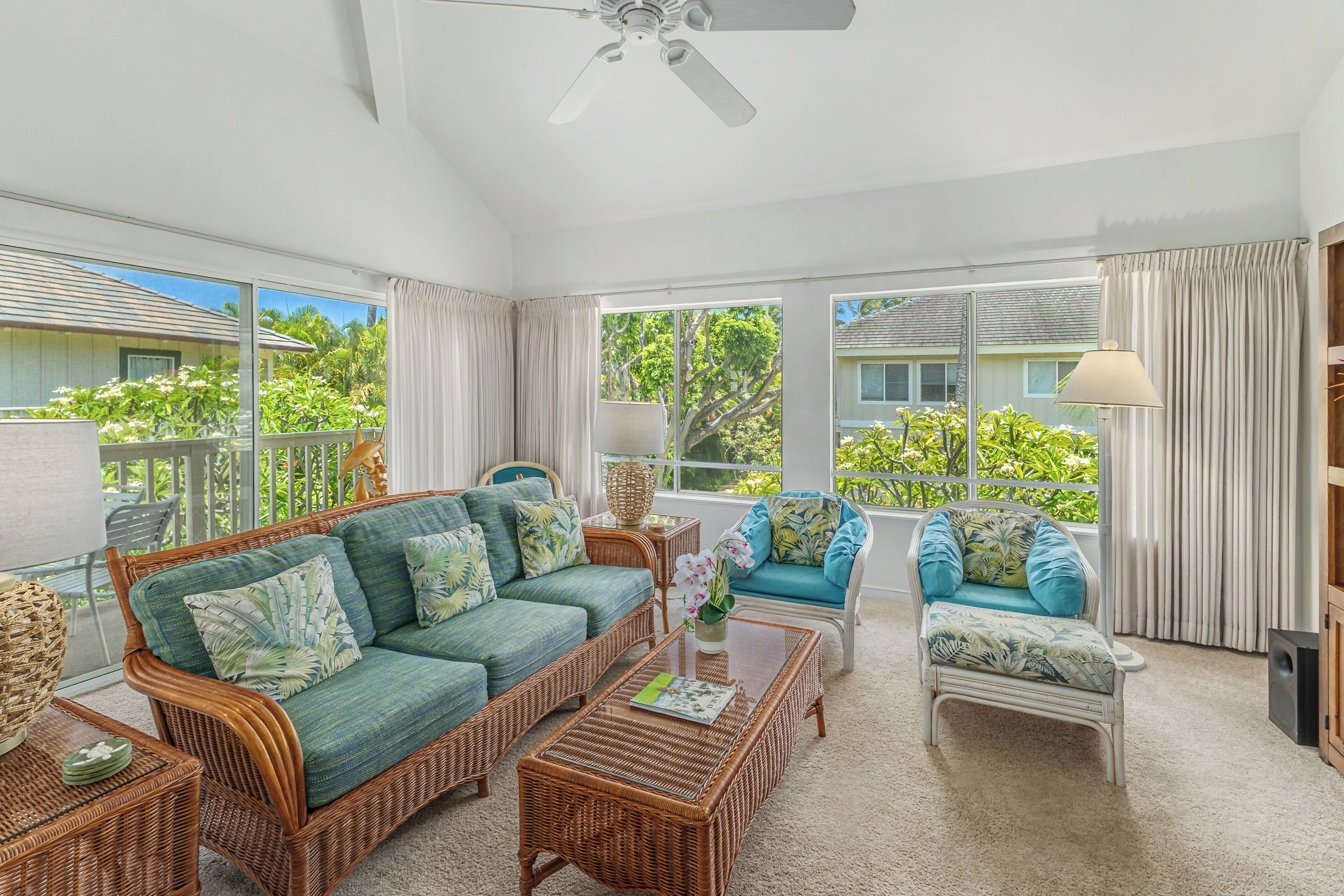 A spacious living area with wicker furniture, large windows, and a ceiling fan.