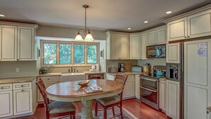 A kitchen with a central island, wooden chairs, a dining table, and a window with a view of greenery. - 77 Plantation Dr - Walk to Harbour Town or Bike ride to Beach. (Hilton Head Island)