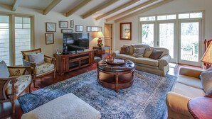 A spacious living room with a large TV, comfortable seating, and a view through large windows. - 77 Plantation Dr - Walk to Harbour Town or Bike ride to Beach. (Hilton Head Island)