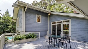 A deck with a glass table and chairs, a pool in the background, and a house with grey siding and a white door. - 77 Plantation Dr - Walk to Harbour Town or Bike ride to Beach. (Hilton Head Island)