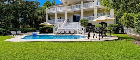 A two-story building with a swimming pool, outdoor seating, and a white picket fence.