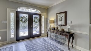 Un couloir avec une porte en bois sombre, une console ornée d’objets décoratifs, une lampe et une œuvre d’art encadrée accrochée au mur.