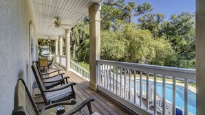 Une terrasse extérieure couverte, dotée de chaises et d’une table en bois, qui offre une vue sur une piscine et une végétation luxuriante.