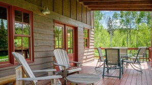 Puuinen mökki, jossa on kuisti, jossa on Adirondack-tyylisiä tuoleja ja pöytä.