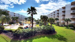 Une cour d’hôtel avec une piscine, des palmiers et un espace délimité par une clôture.