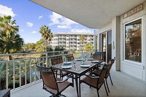 Un balcone con tavolo apparecchiato per mangiare, circondato da sedie, con vista su un edificio con numerosi balconi e palme.