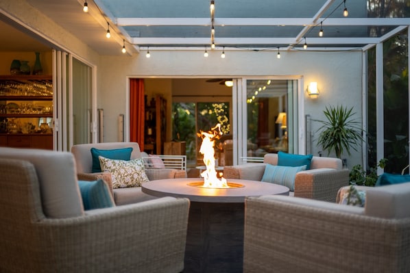 Un espace extérieur accueillant, aménagé avec des meubles en osier, un foyer central et une terrasse fermée par des baies vitrées.